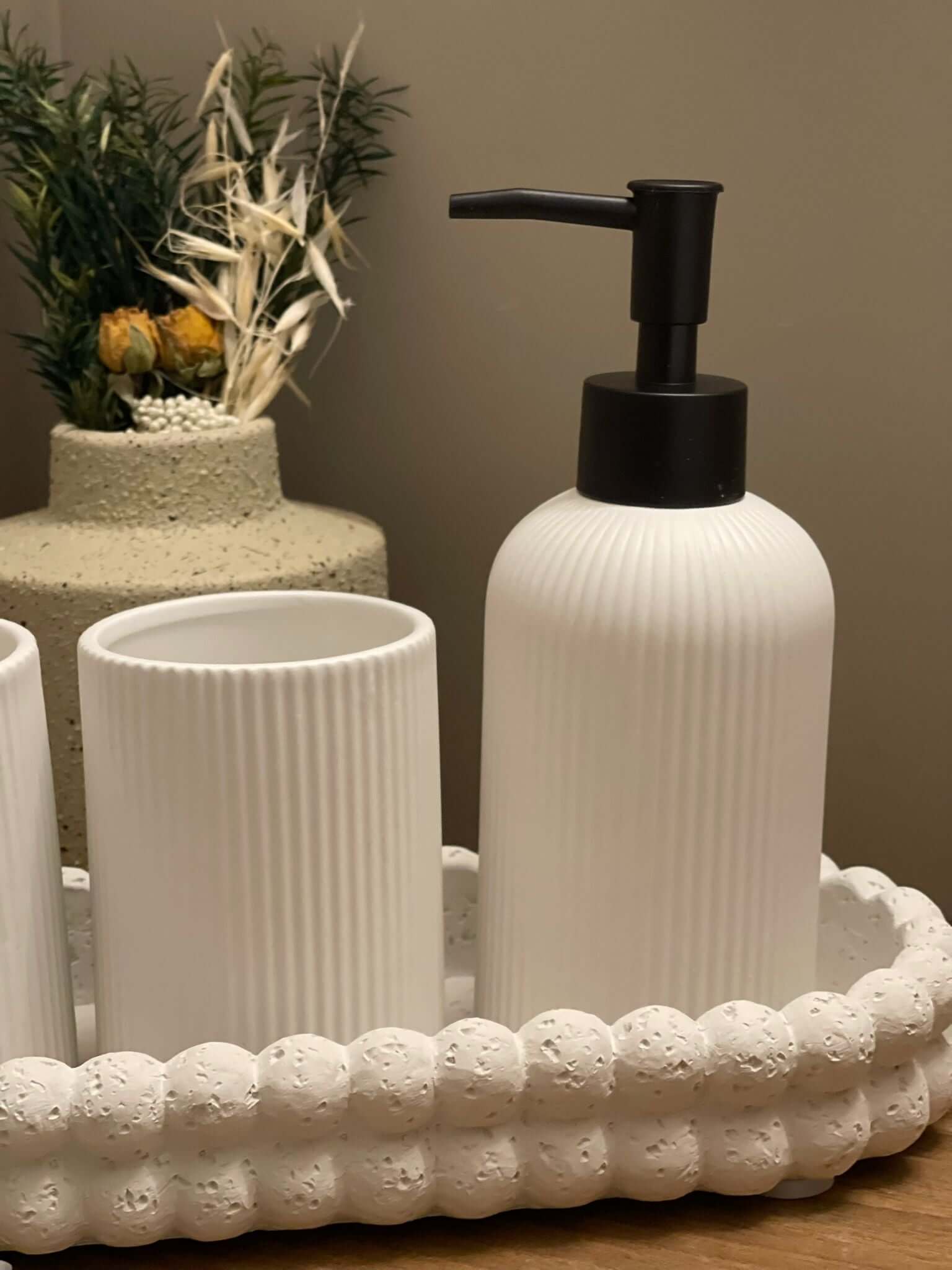 Elegant white striped ceramic bathroom set with liquid soap dispenser, matching cups, and oval tray on wooden surface, harmonious modern design.