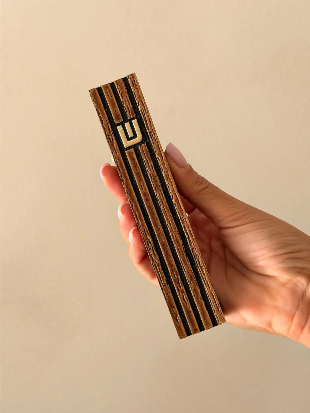 בית מזוזה רידג' בגימור עץ עם פסים שחורים ואות למ"ד מוזהבת - מבט חזיתי ביד בזווית קלה