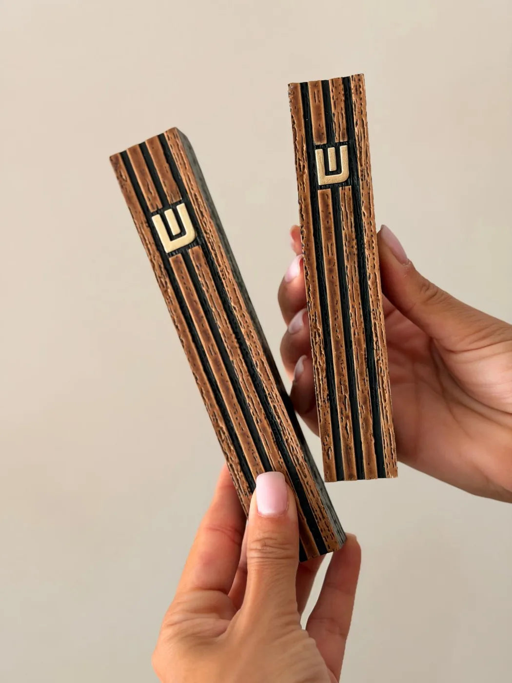 שני בתי מזוזה רידג' בגימור עץ עם פסים שחורים מוחזקים יחד ביד להשוואת שני הגדלים