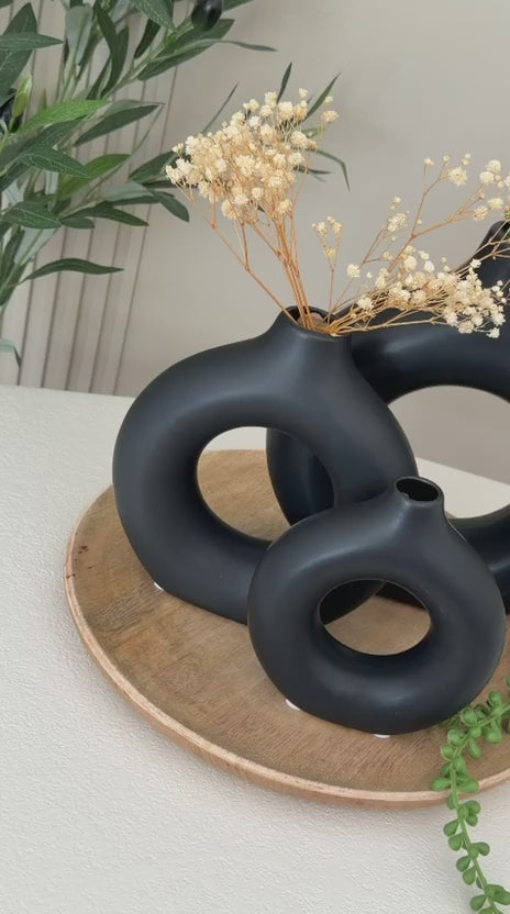 שני אגרטלים שחורים עגולים עם פרחים מיובשים מונחים על מגש עץ דקורטיבי
